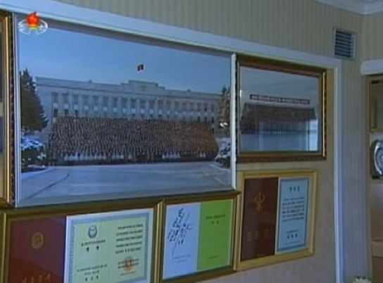 A copy of a December 2012 commemorative photograph (L) of members of the DPRK leadership and personnel involved in the 12 December 2012 launch of the U'nha-3, seen in a resident of the U'nha Scientists' Street (Photo: KCTV screengrab).